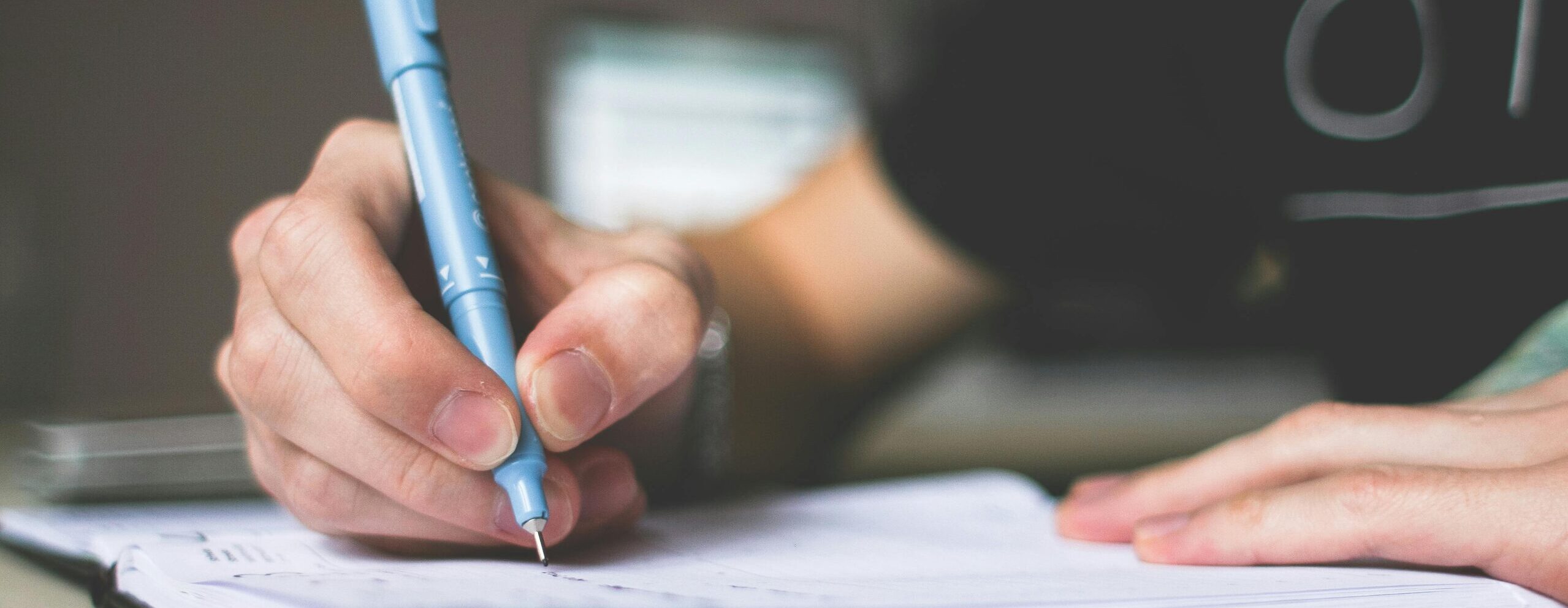 Close-up of hand writing in notebook using a blue pen, focus on creativity.